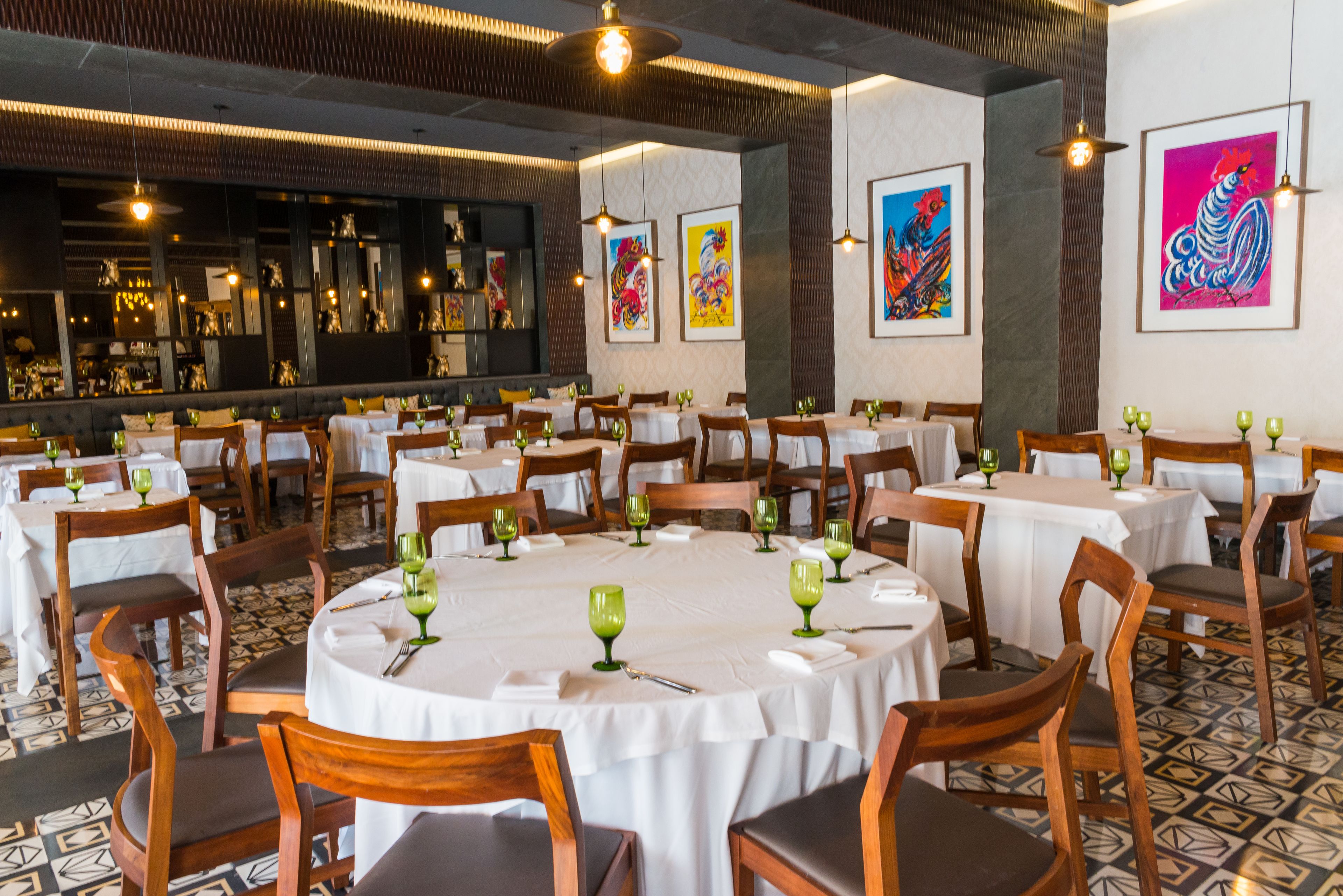 A restaurant with round tables, chairs, and green wine glasses.