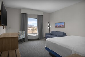 A hotel room with a bed, a desk, a chair, a sofa, a window with curtains, a painting, and a flat-screen TV. - Hampton Inn & Suites Colorado Springs/I-25 South (Colorado Springs)
