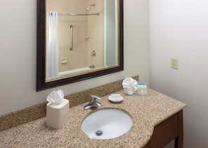 Une salle de bain dotée d’un comptoir en granit, d’un lavabo, d’un miroir, d’un distributeur de serviettes et d’articles de toilette.
