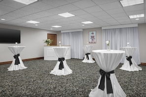 A conference room with carpeted flooring, white tables with black sashes, a flat-screen TV, a wooden cabinet, and a framed picture on the wall. - Hampton Inn & Suites Colorado Springs/I-25 South (Colorado Springs)