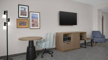 Una habitación con una mesa redonda, una silla estampada, un armario con microondas, un sillón azul y tres cuadros en la pared.