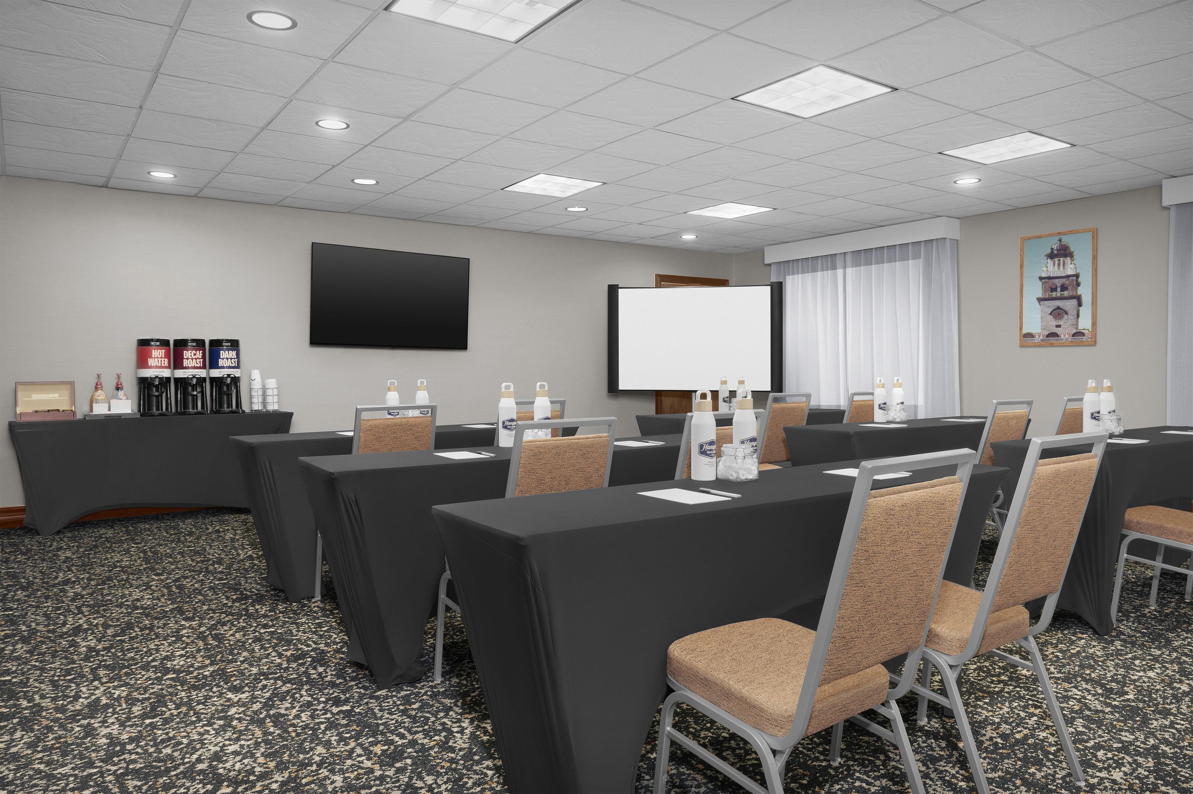 A conference room with tables, chairs, a projector screen, and a television.