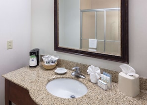 Une salle de bain dotée d’un comptoir en granit, d’un lavabo, d’un miroir, d’un distributeur de serviettes et d’articles de toilette.