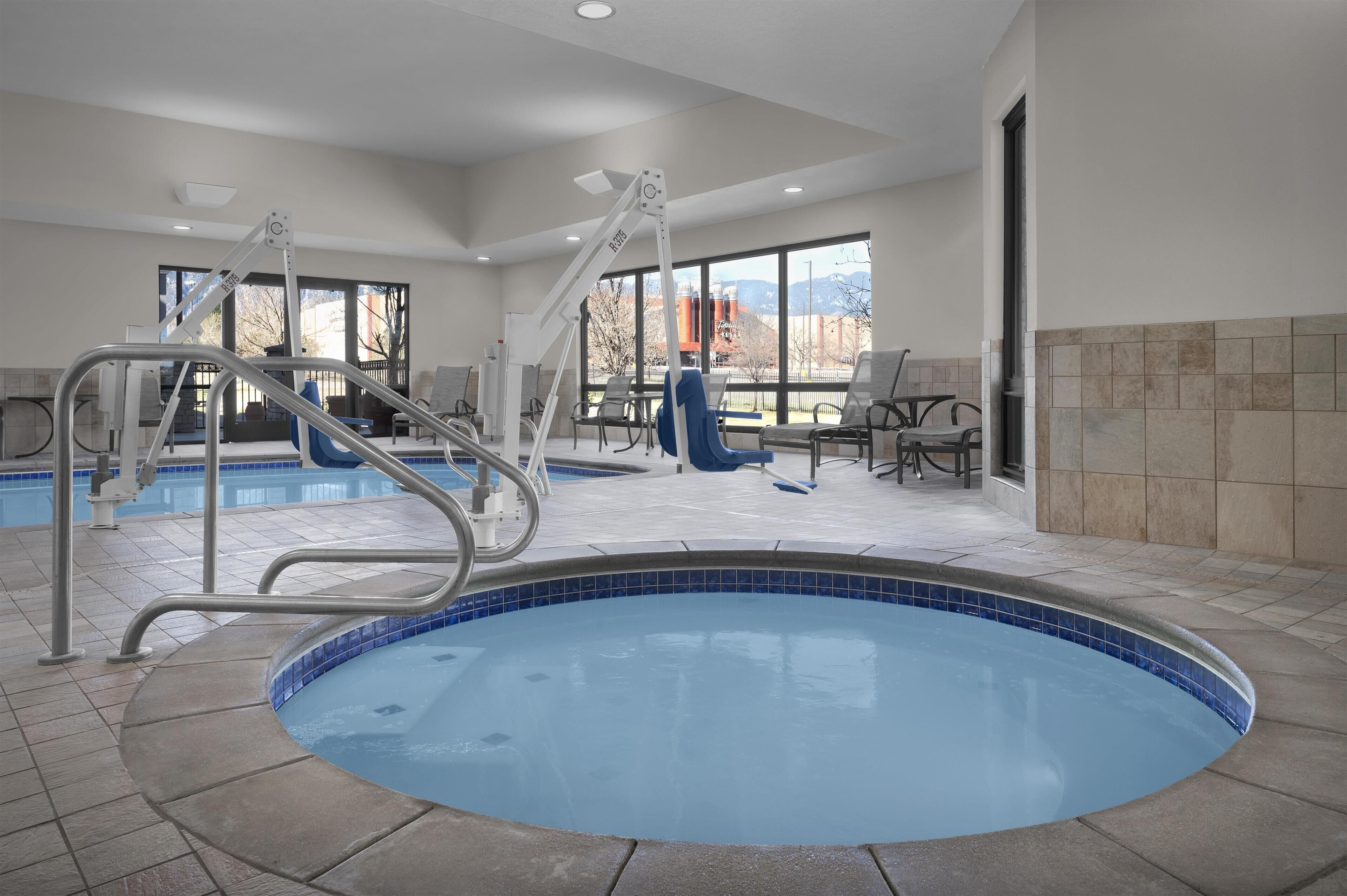 A pool area with a hot tub, a lounge chair, and a table with chairs.