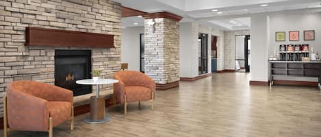 A spacious lobby with a brick fireplace, two armchairs, a round table, and a coffee station.