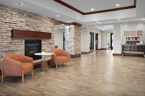 A spacious lobby with a brick fireplace, two armchairs, a round table, and a coffee station. - Hampton Inn & Suites Colorado Springs/I-25 South (Colorado Springs)