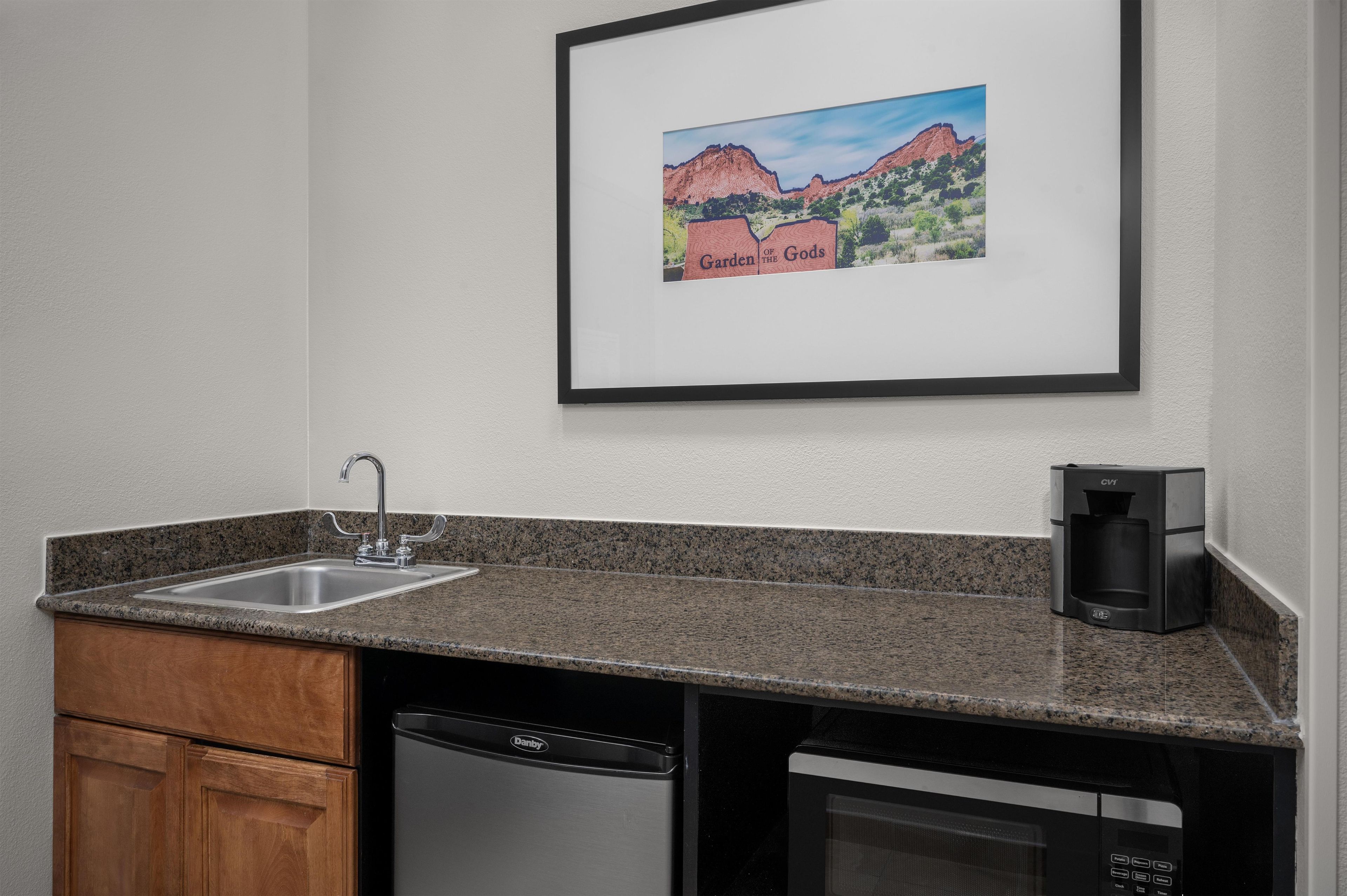 A kitchen with granite countertops, a dishwasher, a coffee maker, and a framed picture of a mountain landscape.