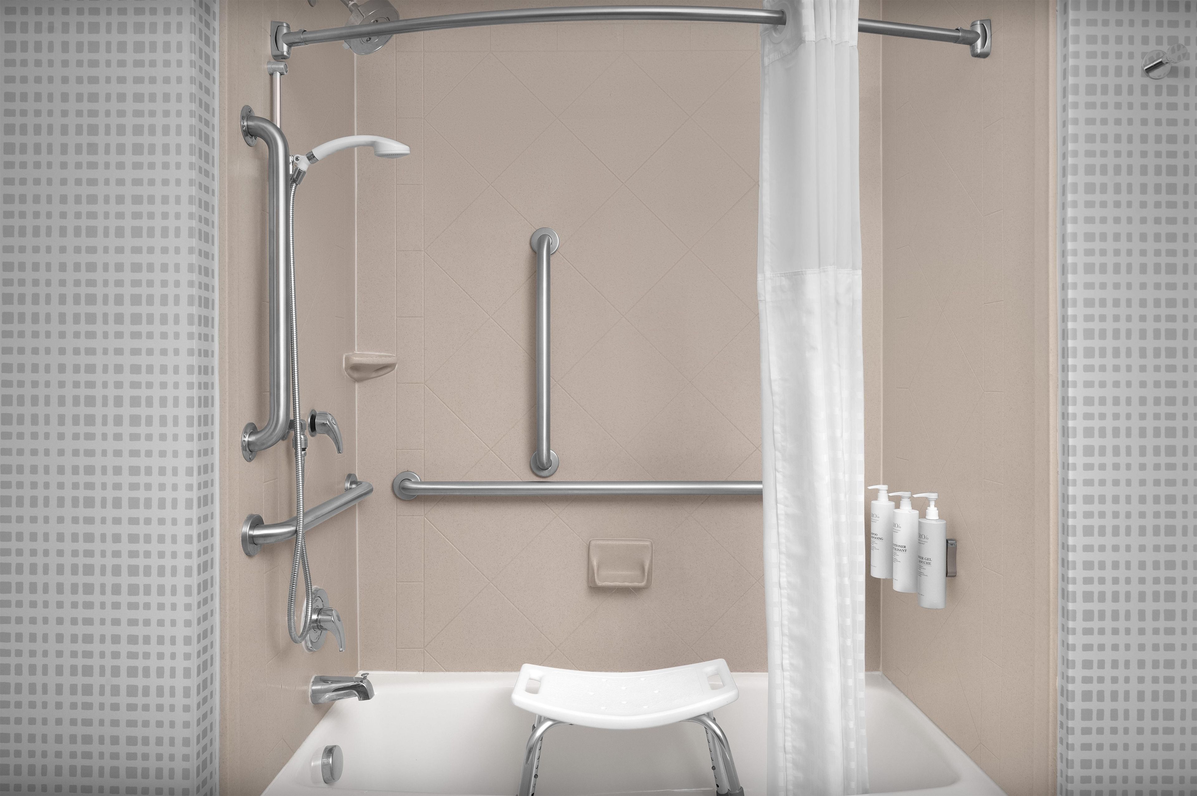 A bathroom with a shower, grab bars, a step stool, and toiletries on the wall.
