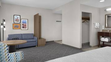 A hotel room with a bed, a sofa, a small table, a chair, a bathroom, and framed pictures on the wall.
