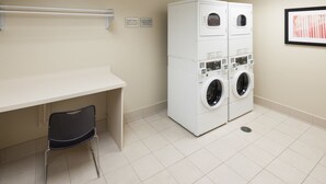 A laundry room with a white washing machine and dryer, a chair, and a sign indicating cycle times. - Hampton Inn & Suites Colorado Springs/I-25 South (Colorado Springs)