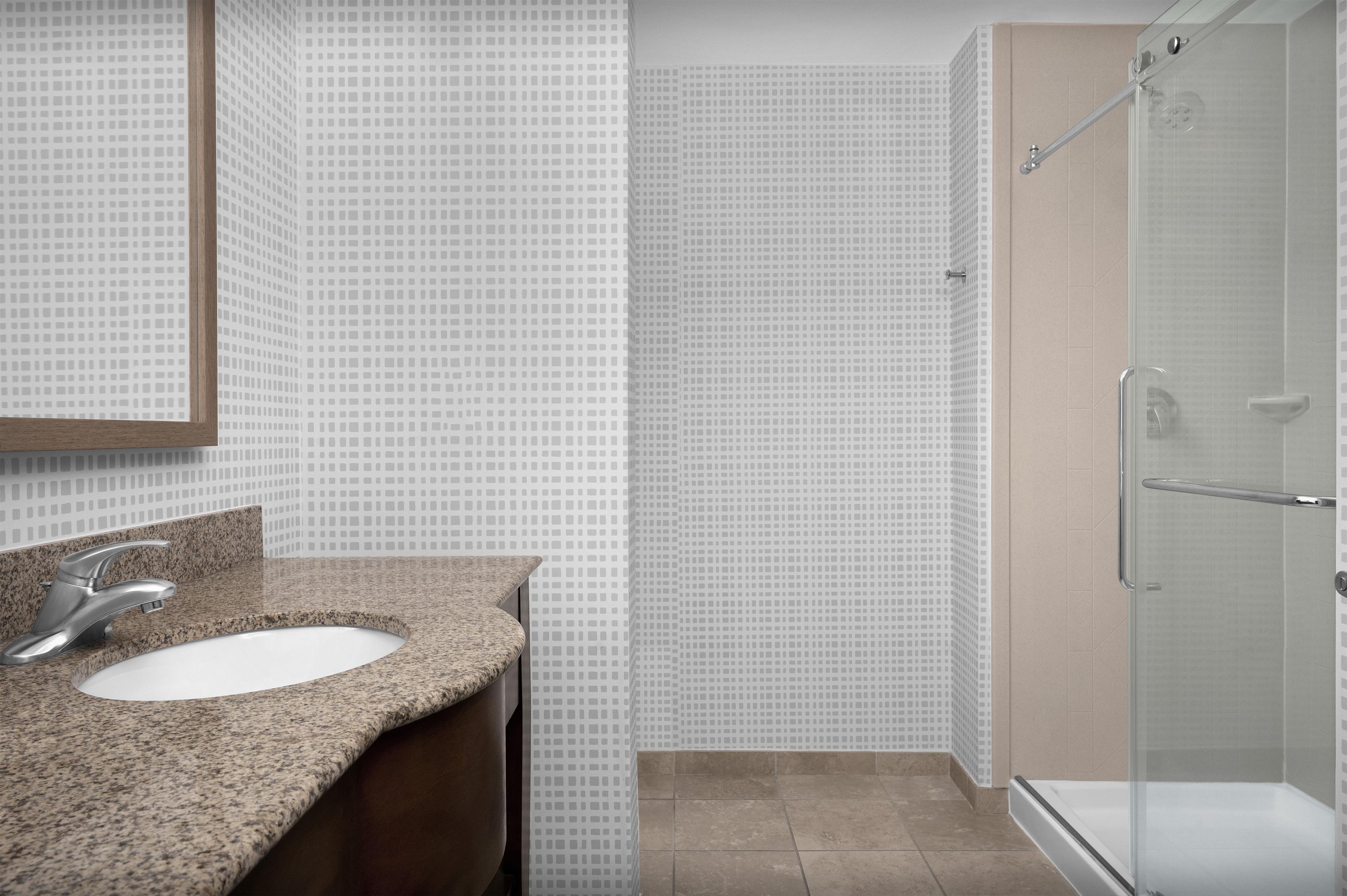 A bathroom with a granite countertop, a sink, a mirror, and a glass shower enclosure.
