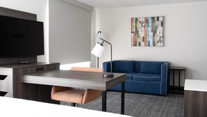 Una habitación de hotel moderna con una televisión de pantalla plana, una mesa de comedor, un sofá, una lámpara y un cuadro abstracto colorido en la pared.