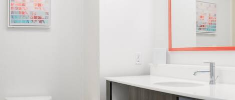 A modern bathroom with a toilet, sink, mirror, and a framed picture on the wall.