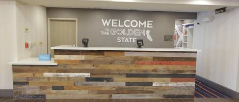 Un mostrador de recepción con un cartel que dice 'Welcome to the Golden State', el logotipo de Hilton y un cartel que dice 'Suite Shop'.