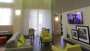 Un vestíbulo amplio con un sofá gris, sillones amarillos, un ventilador de techo y un televisor en la pared.