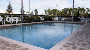 A swimming pool with a brick border, surrounded by white chairs and a fence. - Hampton Inn & Suites Orlando-John Young Pkwy/S. Park (Orlando)