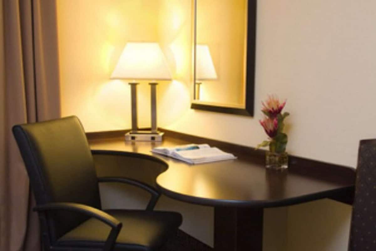 Ein Hotelzimmer mit Schreibtisch, zwei Stühlen, einer Lampe, einem Spiegel und einer kleinen Vase mit Blumen.