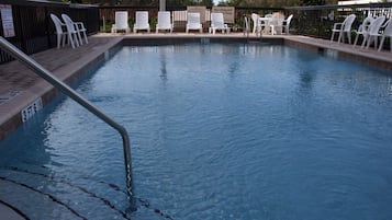 Une piscine dont la profondeur maximale est indiquée à 1,5 mètre, entourée de chaises longues blanches et agrémentée d’un panneau indiquant l’absence de sauveteur.