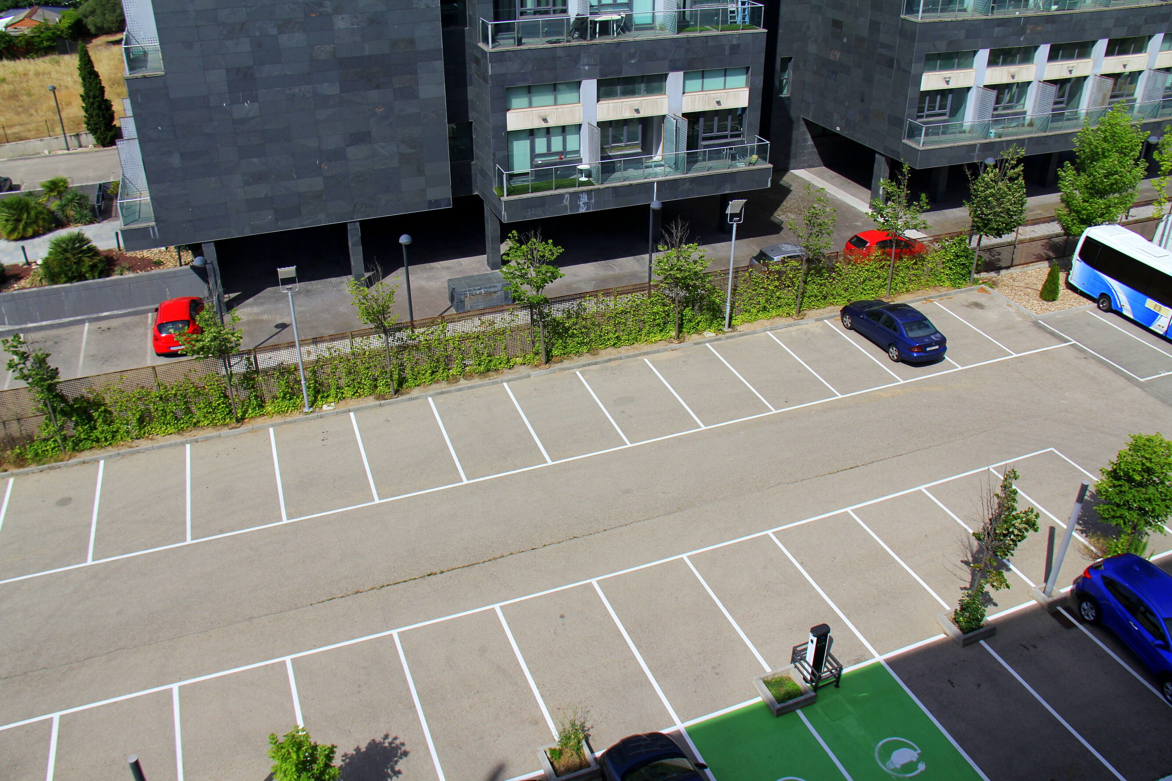 A parking lot with multiple cars and a bus, surrounded by modern buildings with balconies and large windows.