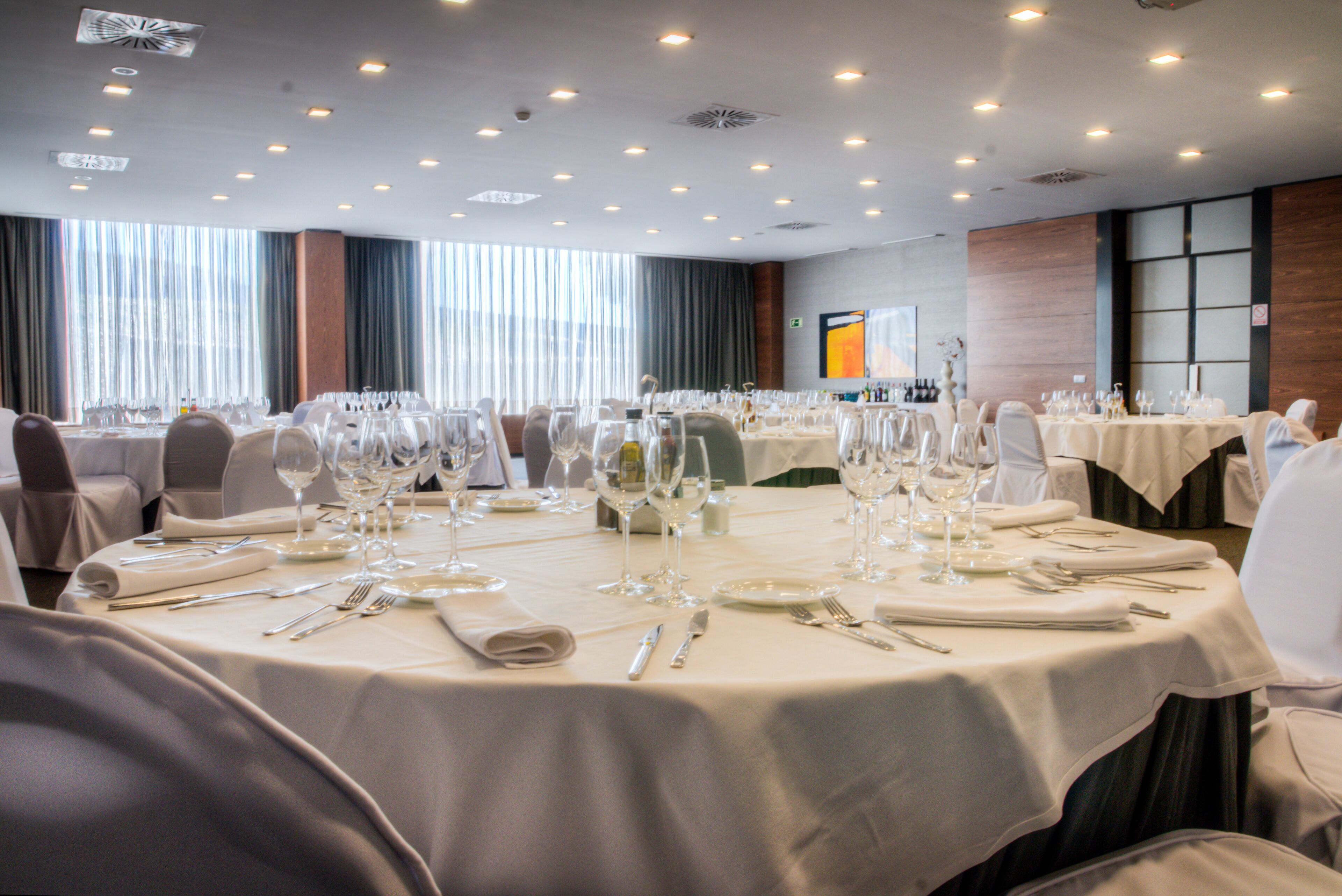 Un salón de banquetes con mesas redondas dispuestas para comer, con cubiertos, platos y copas de vino.