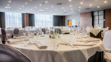 Un salón de banquetes con mesas redondas dispuestas para comer, con cubiertos, platos y copas de vino.