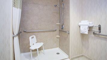 A wheelchair-accessible shower area with a white chair, grab bars, and a towel rack.