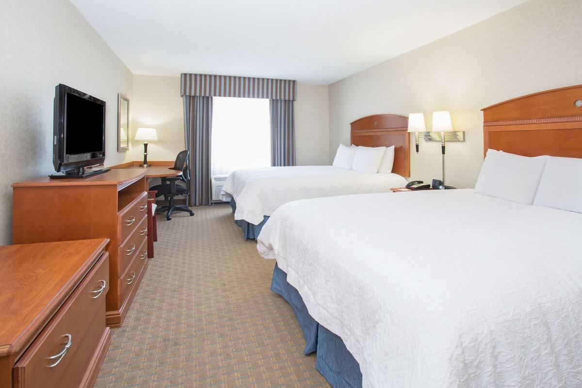 A hotel room with two beds, a desk with a television, a chair, and a lamp.