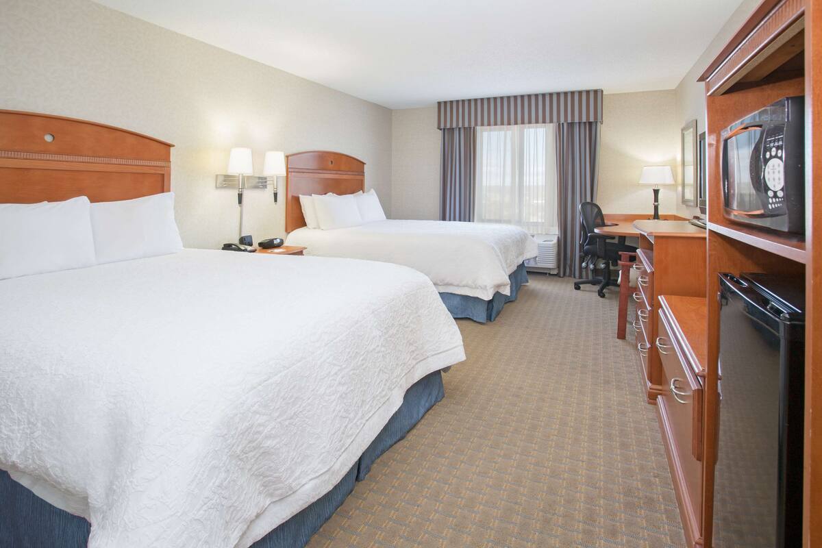 A hotel room with two beds, a desk, a chair, a microwave, and a television.