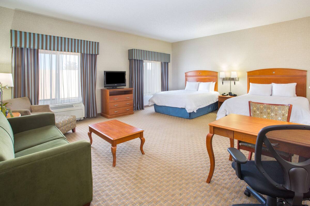 A hotel room with a bed, a desk, a chair, a television, and a sofa.