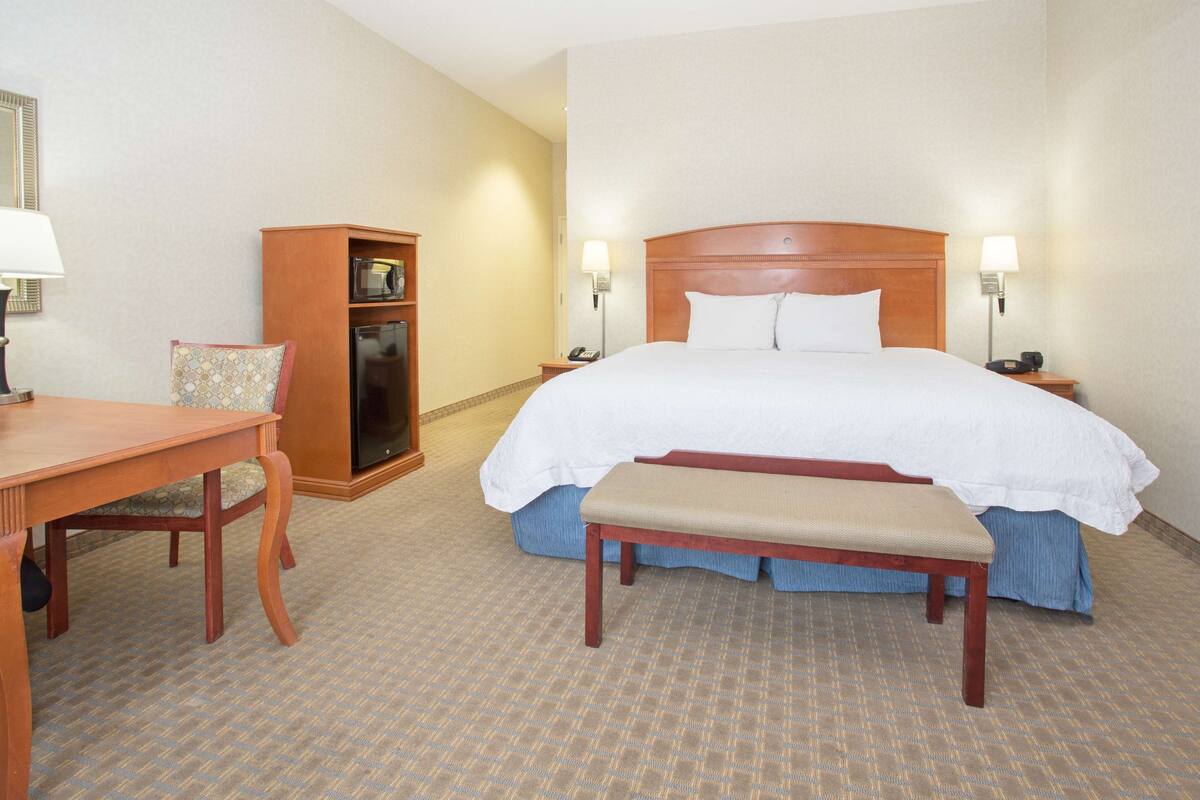 A hotel room with a large bed, a wooden bench, a desk, and a small cabinet.