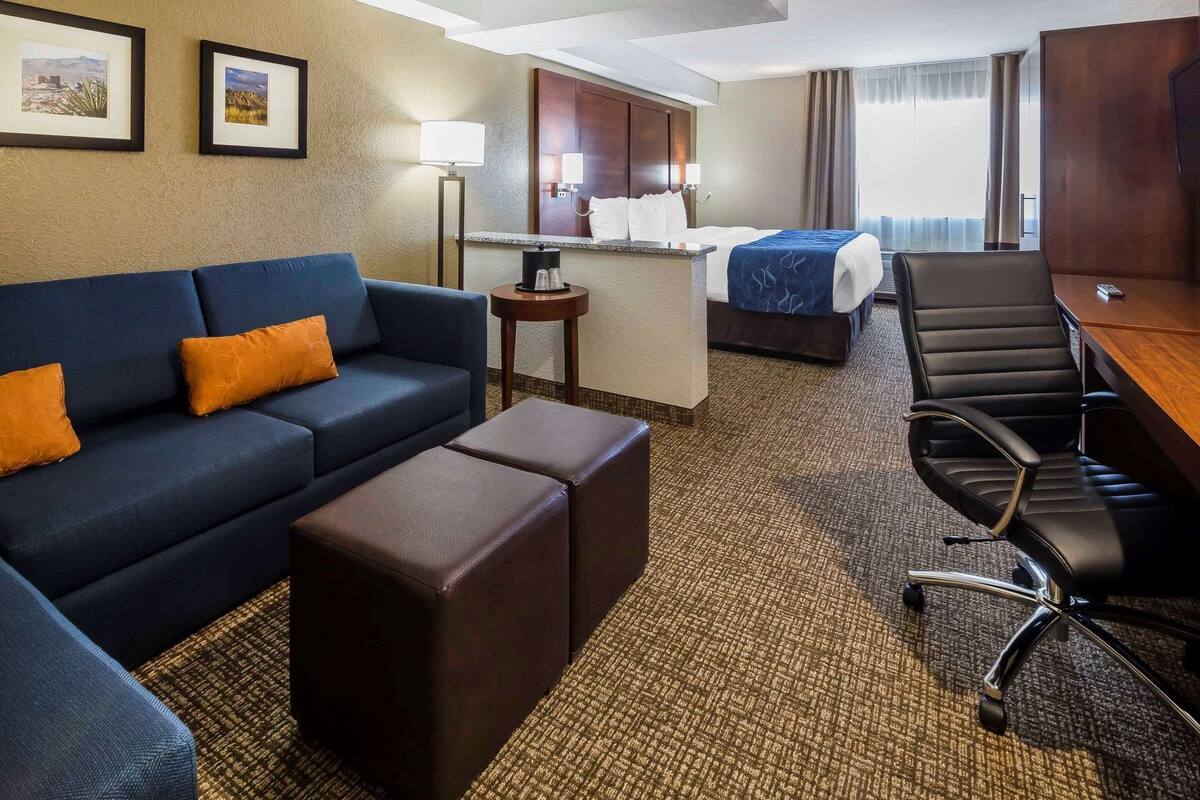A hotel room with a sofa, ottoman, desk, chair, and a bed.