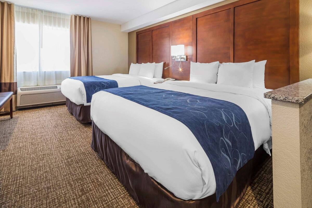 A hotel room with two beds, a desk, and a window with curtains.
