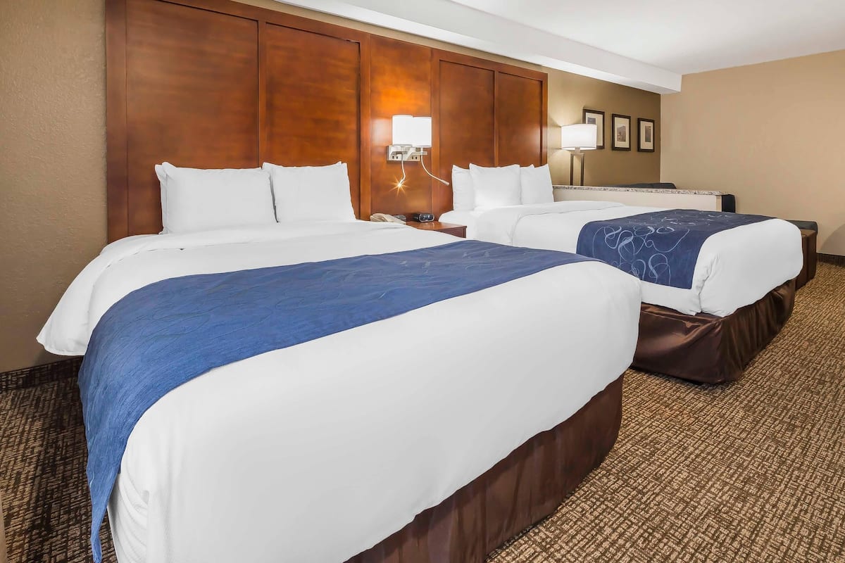 A hotel room with two beds, a wooden headboard, a nightstand with a lamp, and a carpeted floor.
