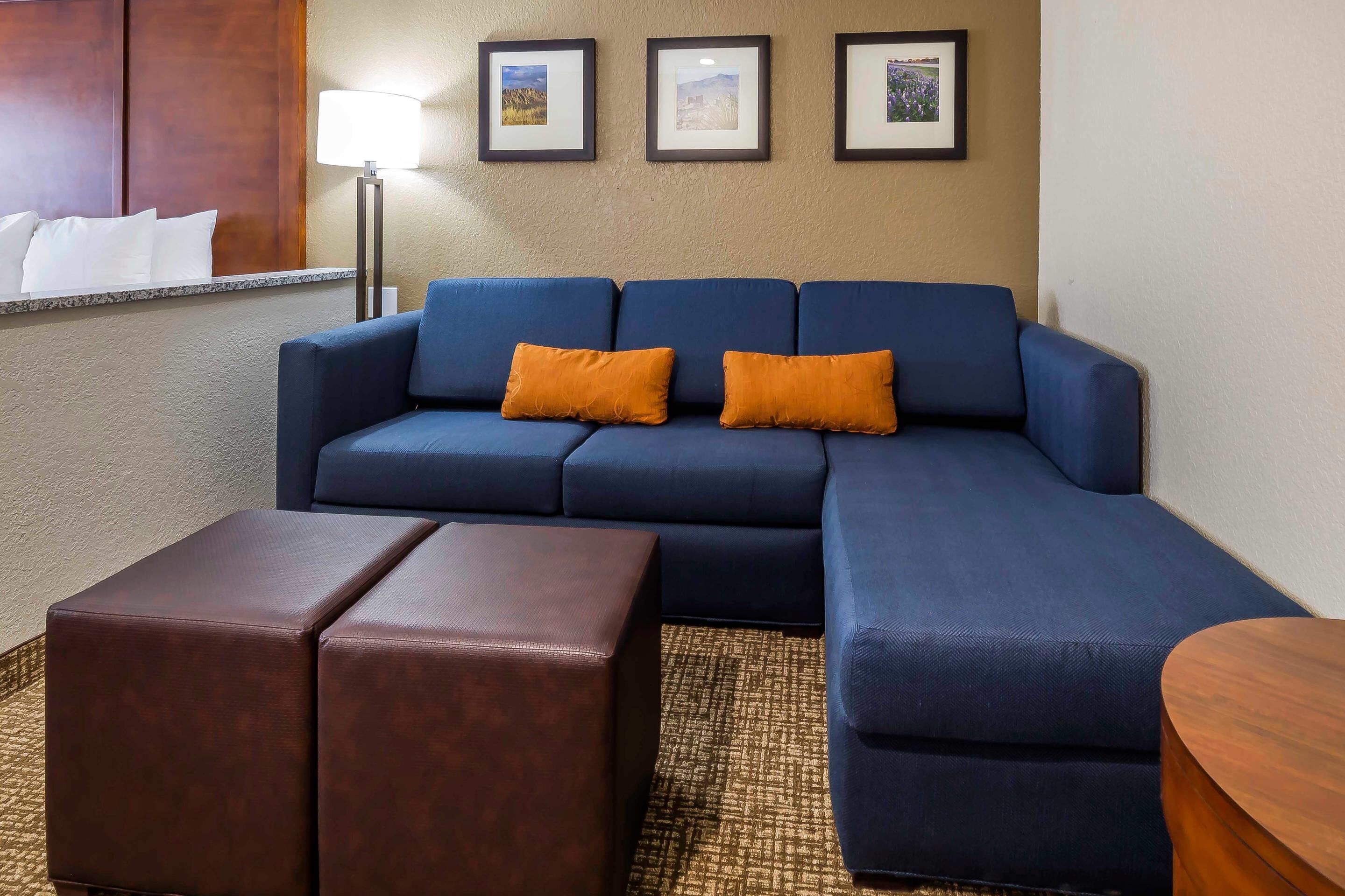 A modern living room with a blue sectional sofa, two brown ottomans, a round wooden side table, and a floor lamp.