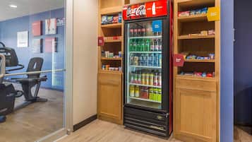 A vending machine with Coca-Cola and a snack shelf, a treadmill, and a glass wall.