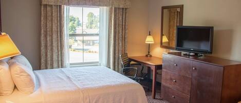 A hotel room with two beds, a desk, a television, a lamp, and a window with curtains.