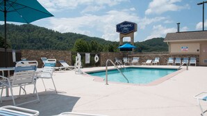 A pool area with lounge chairs and umbrellas, a sign for Hampton Inn by Hilton, and a view of a forested hill. - Hampton Inn Murphy (Murphy)