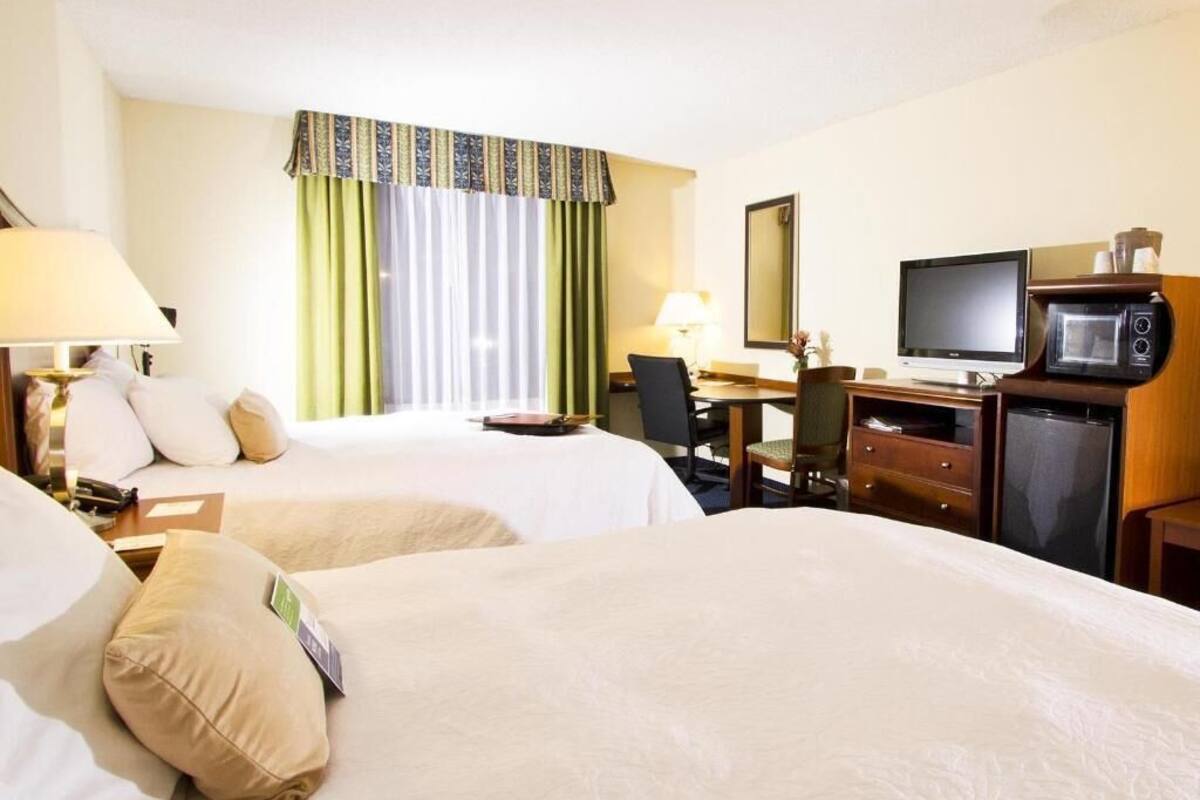 A hotel room with two beds, a desk with a computer, a microwave, and a television.
