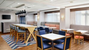 Eine moderne Hotelhalle mit Holzboden, blau-orangen Sitzgelegenheiten und einem Flachbildfernseher an der Wand.