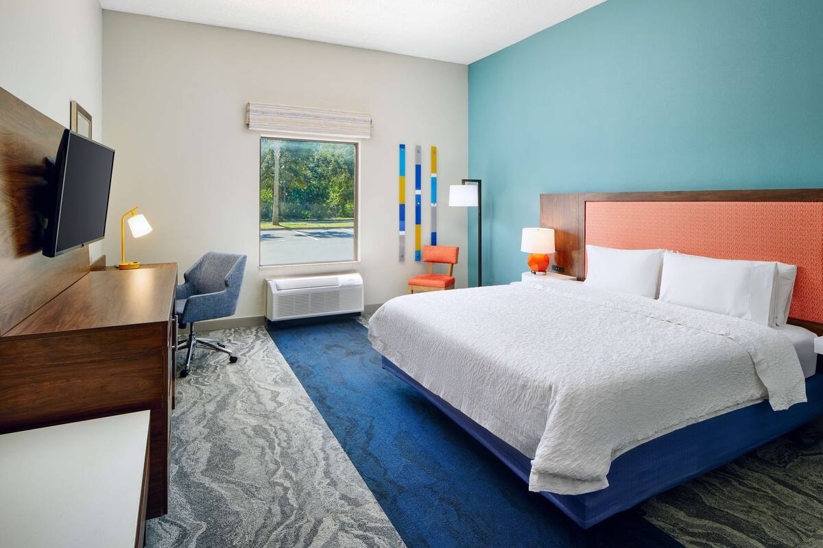 A hotel room with a bed, desk, chair, and a TV.