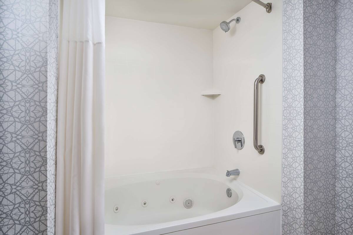 A modern bathroom with a freestanding bathtub, grab bars, and a showerhead.
