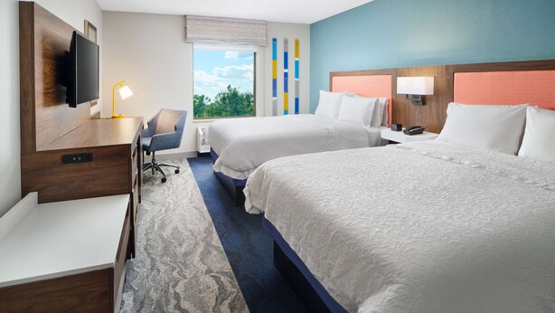 Ein Hotelzimmer mit zwei Betten, einem Schreibtisch, einem Stuhl, einem Fernseher und einem Fenster mit Blick.