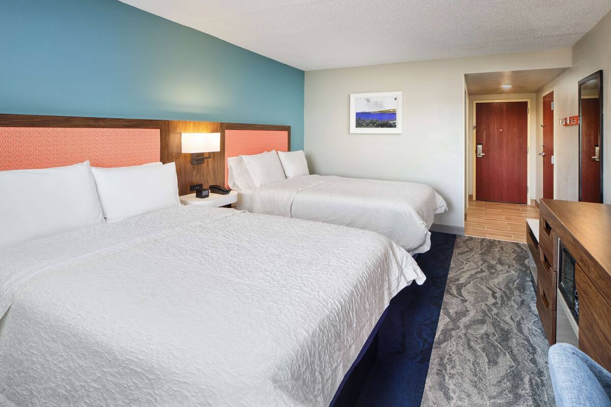 A hotel room with two beds, a nightstand, a desk, and a mirror.
