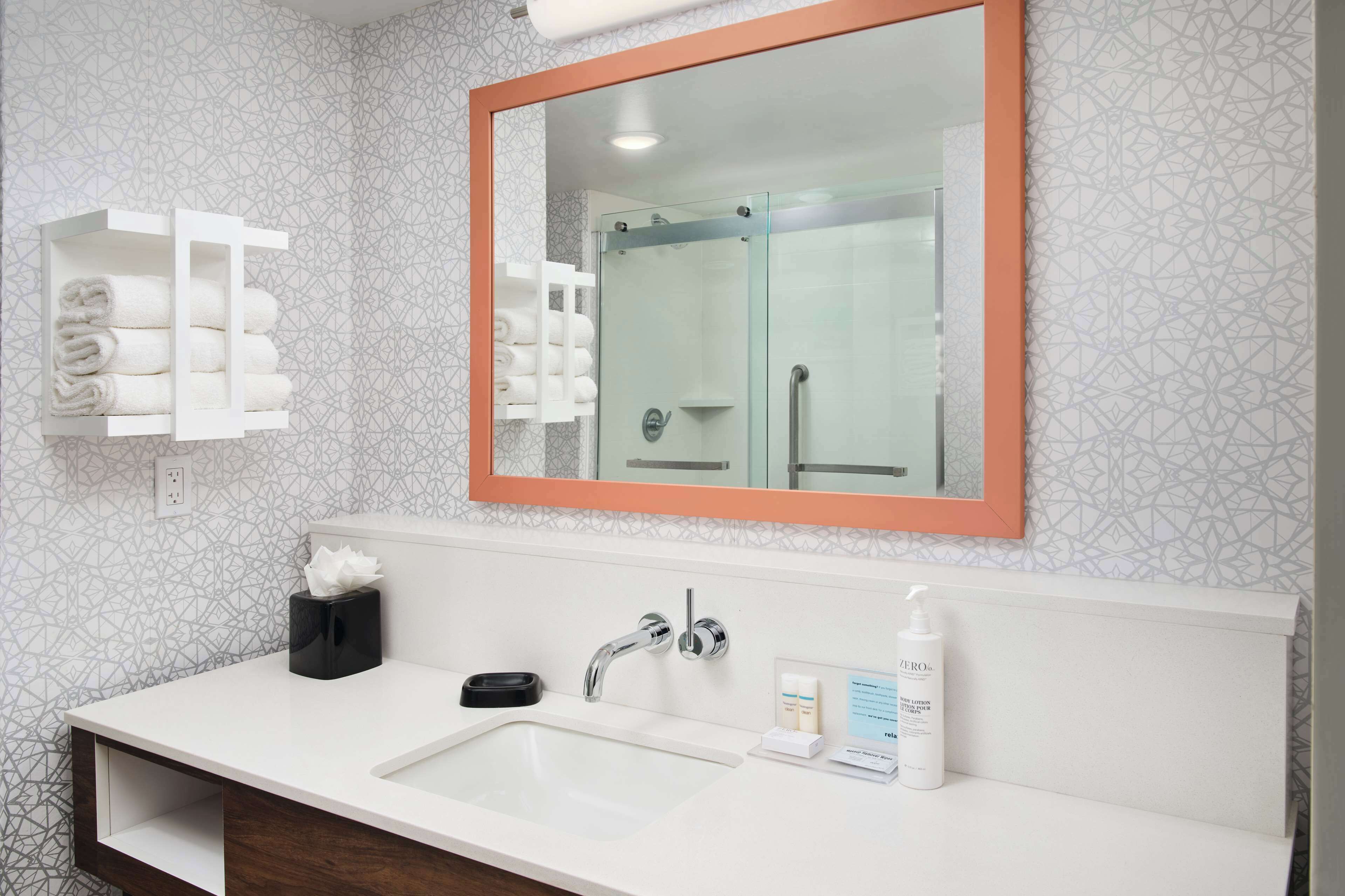 Un baño moderno con un espejo grande, un lavabo blanco y un box de ducha de vidrio.