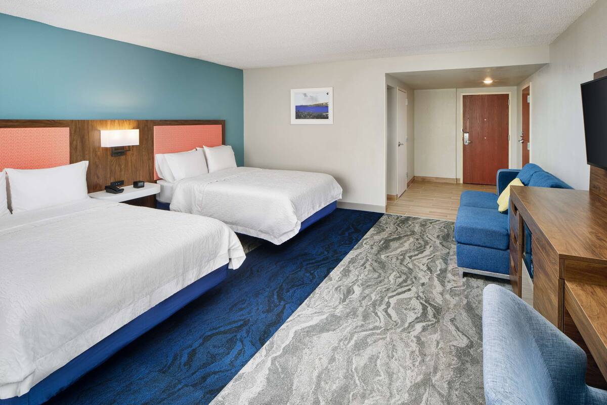 A hotel room with two beds, a desk, a chair, and a TV.