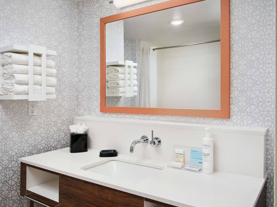 Une salle de bain avec un lavabo blanc, un miroir avec un cadre orange et des distributeurs de serviettes.