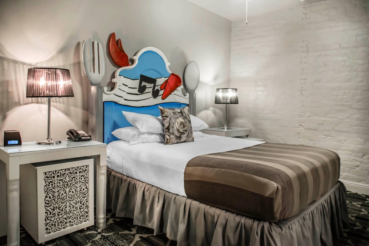 A hotel room with a bed, a nightstand with a lamp, a telephone, and a decorative headboard.