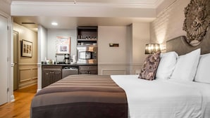 A hotel room with a large bed, a kitchen area with a microwave, and a dining table.