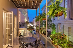 A covered outdoor seating area with a table and chairs, a railing with hanging plants, and a view of a street with buildings.