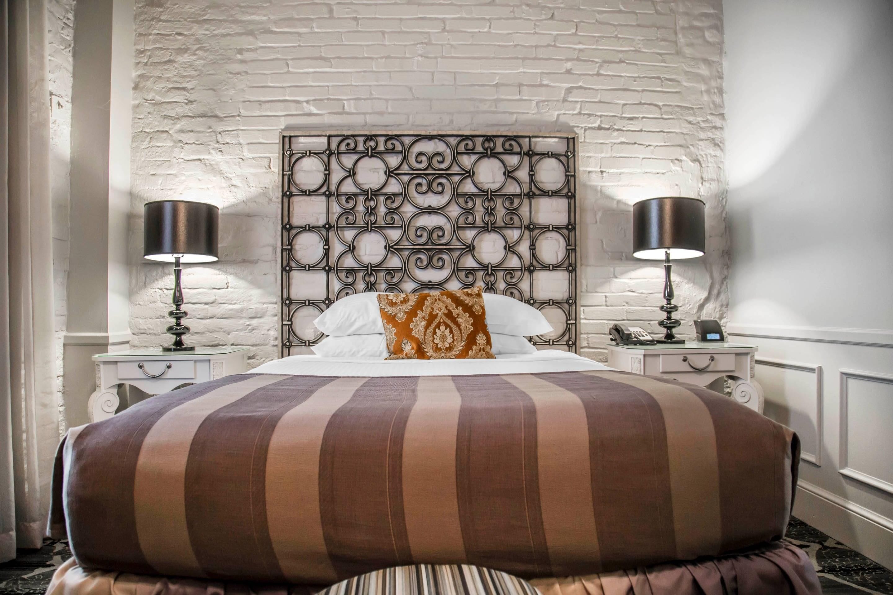 Uma cama com cabeceira estampada, duas mesas de cabeceira com abajures e um edredom listrado.
